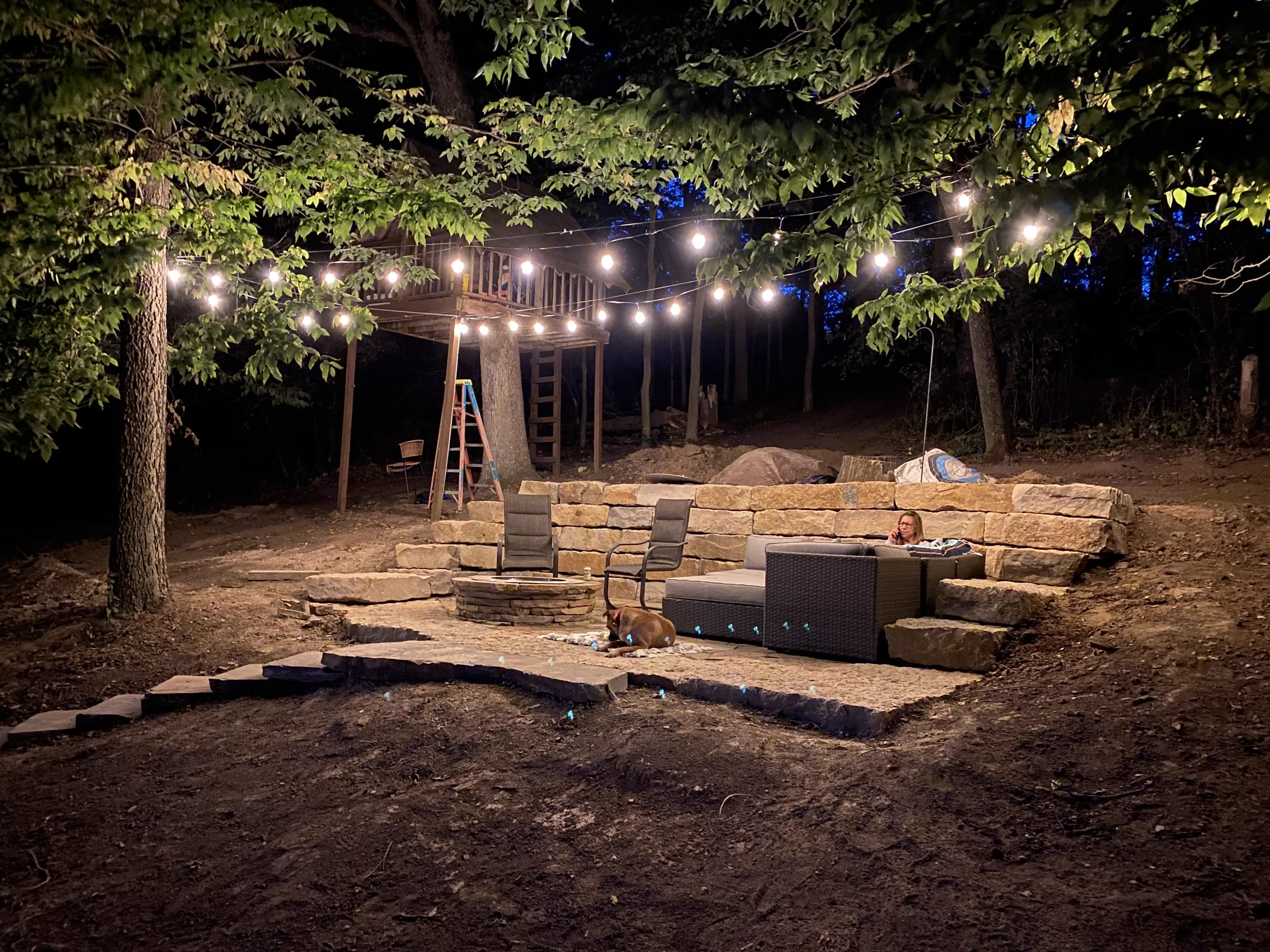 Outdoor living space at night with string lights and stone seating wall