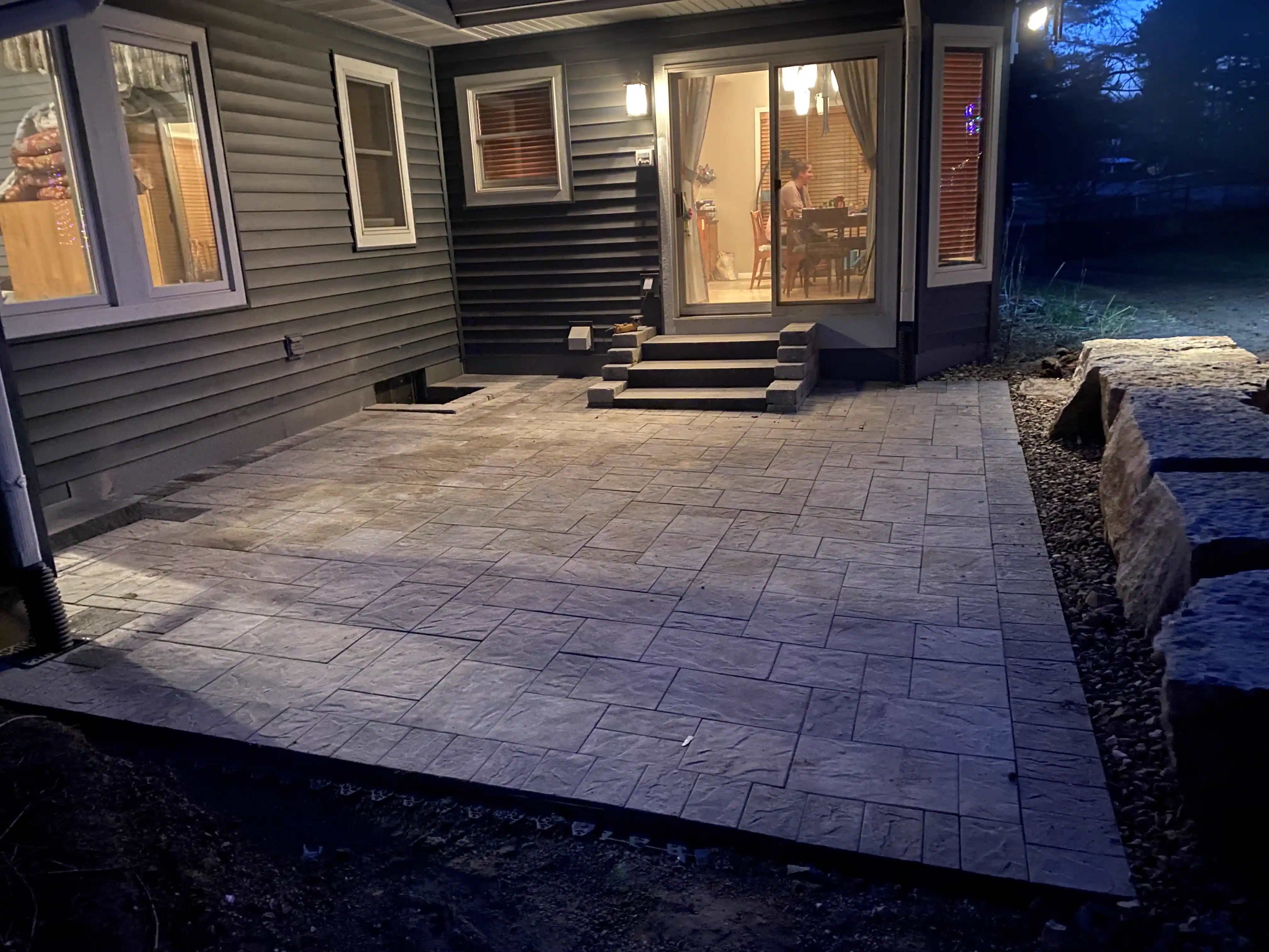 Paver patio illuminated at night behind a residential home